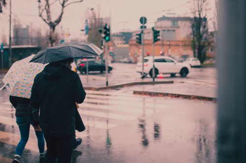 Free People crossing a rainy street intersection in Milan, Italy with umbrellas. Stock Photo