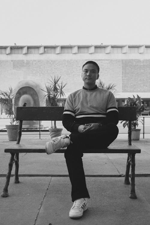 Grayscale Photo of Man Sitting on Wooden Bench