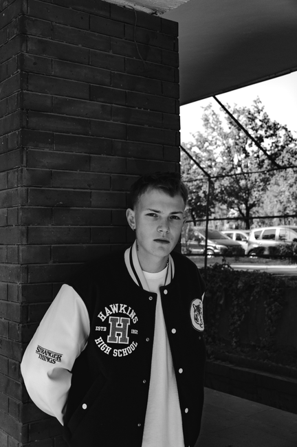 Black and white portrait of a teenager posing in a letterman jacket outdoors.