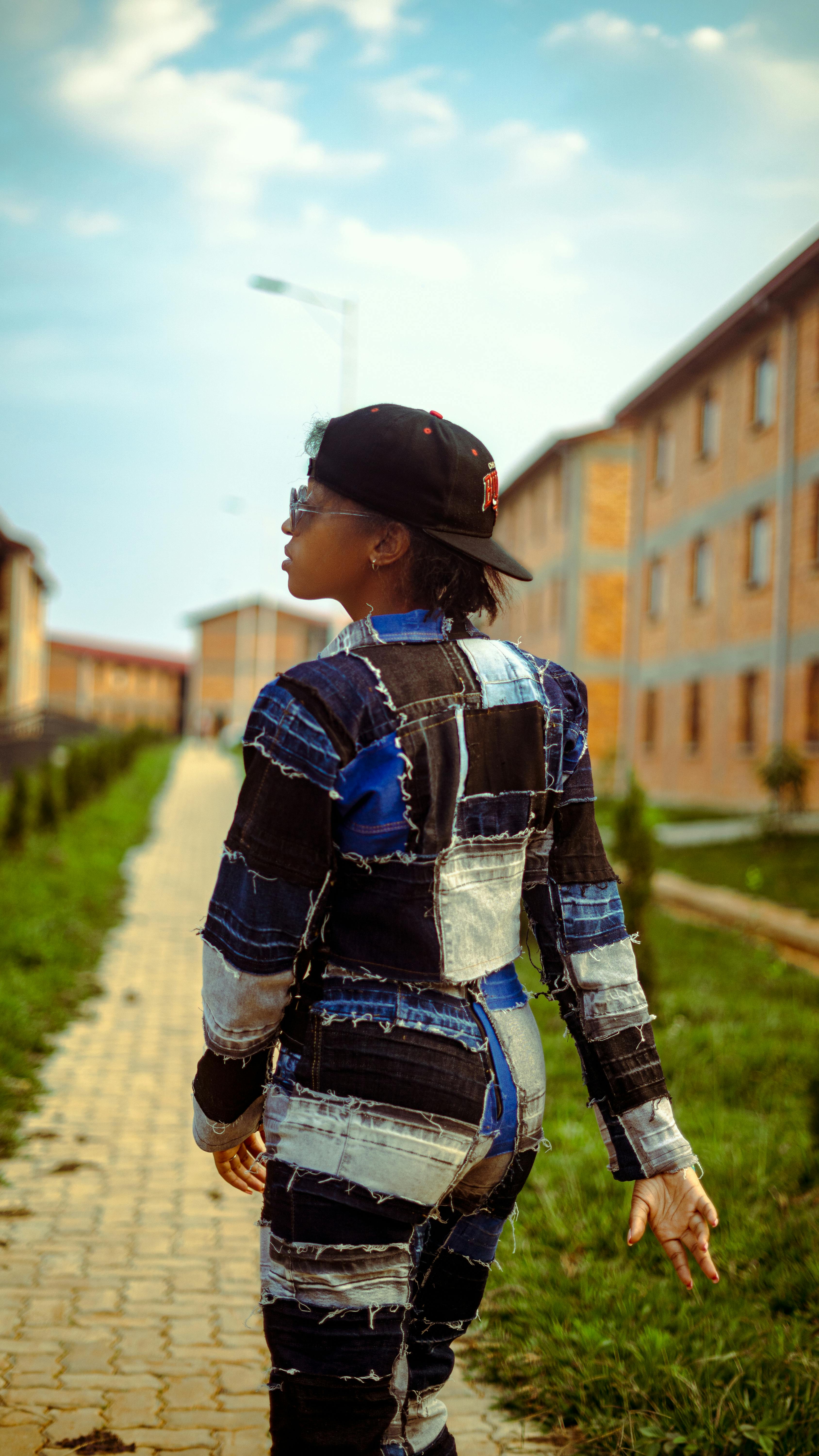 Stylish person in denim jacket and cap walking through modern urban landscape.