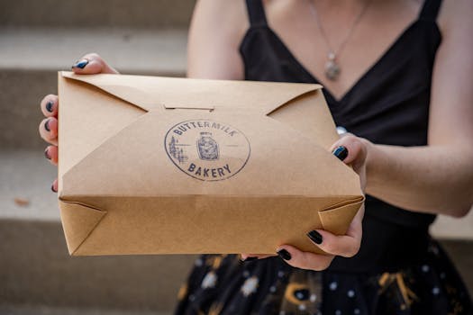 A woman holding a cardboard box from Buttermilk Bakery, offering a close-up view with hands.