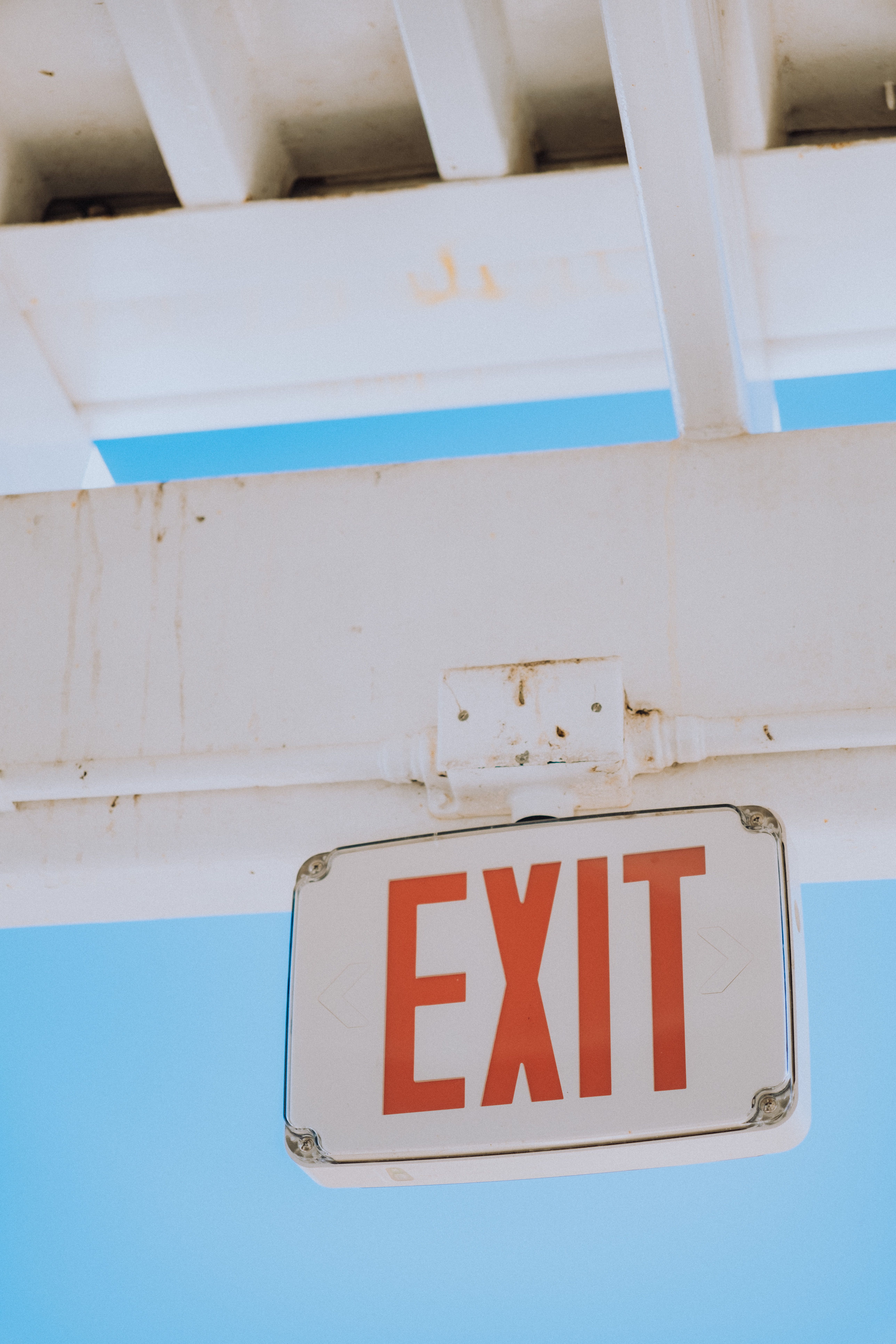 A white and red exit sign against a bright blue sky, symbolizing safety.