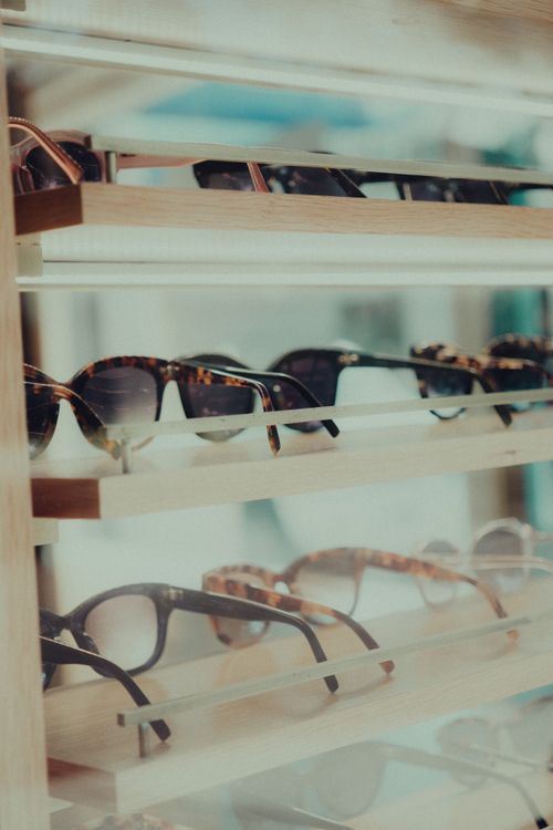 Free Elegant display of various sunglasses on wooden shelves in a retail store. Stock Photo
