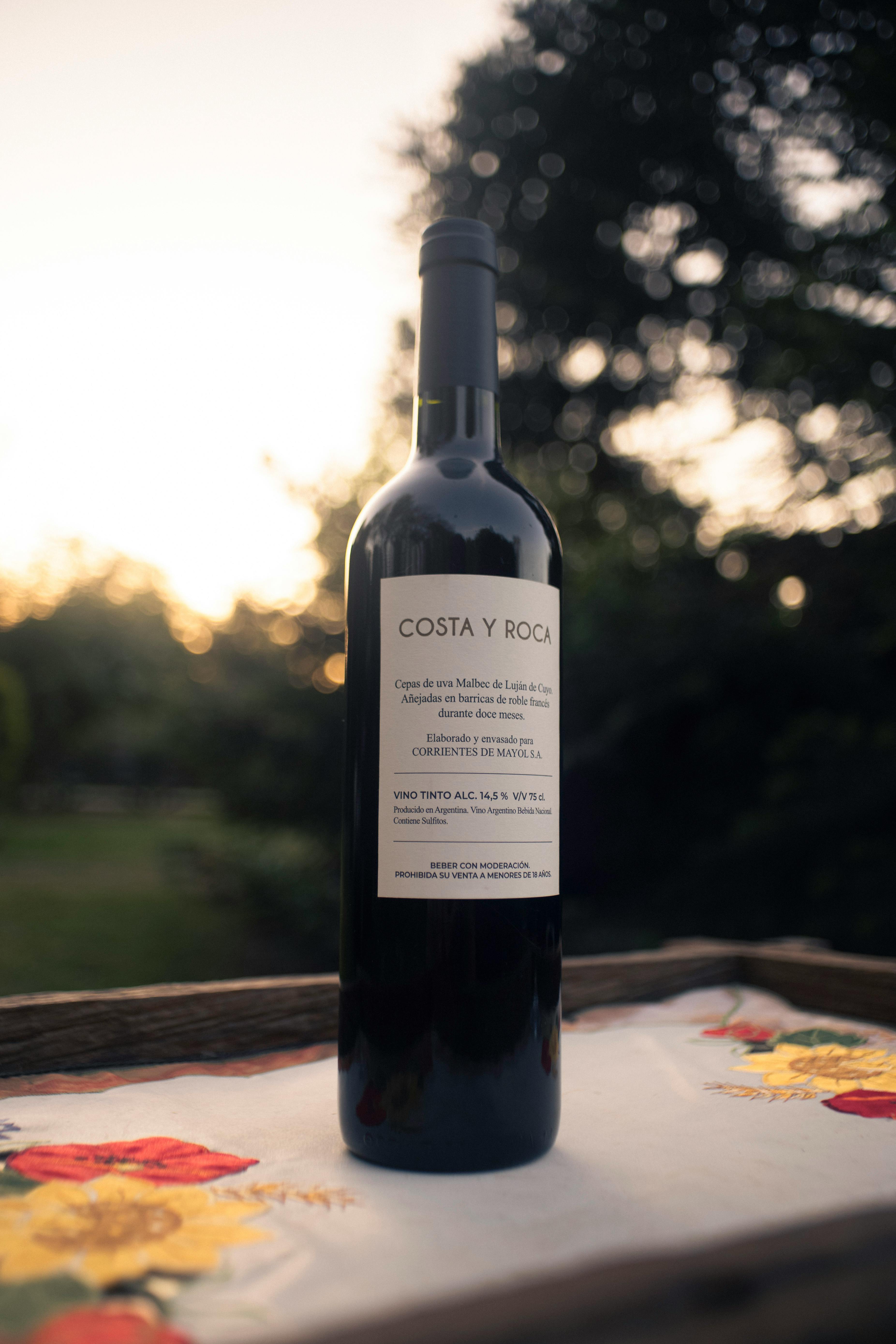 A wine bottle on a table with a sunset backdrop, creating a serene outdoor setting.