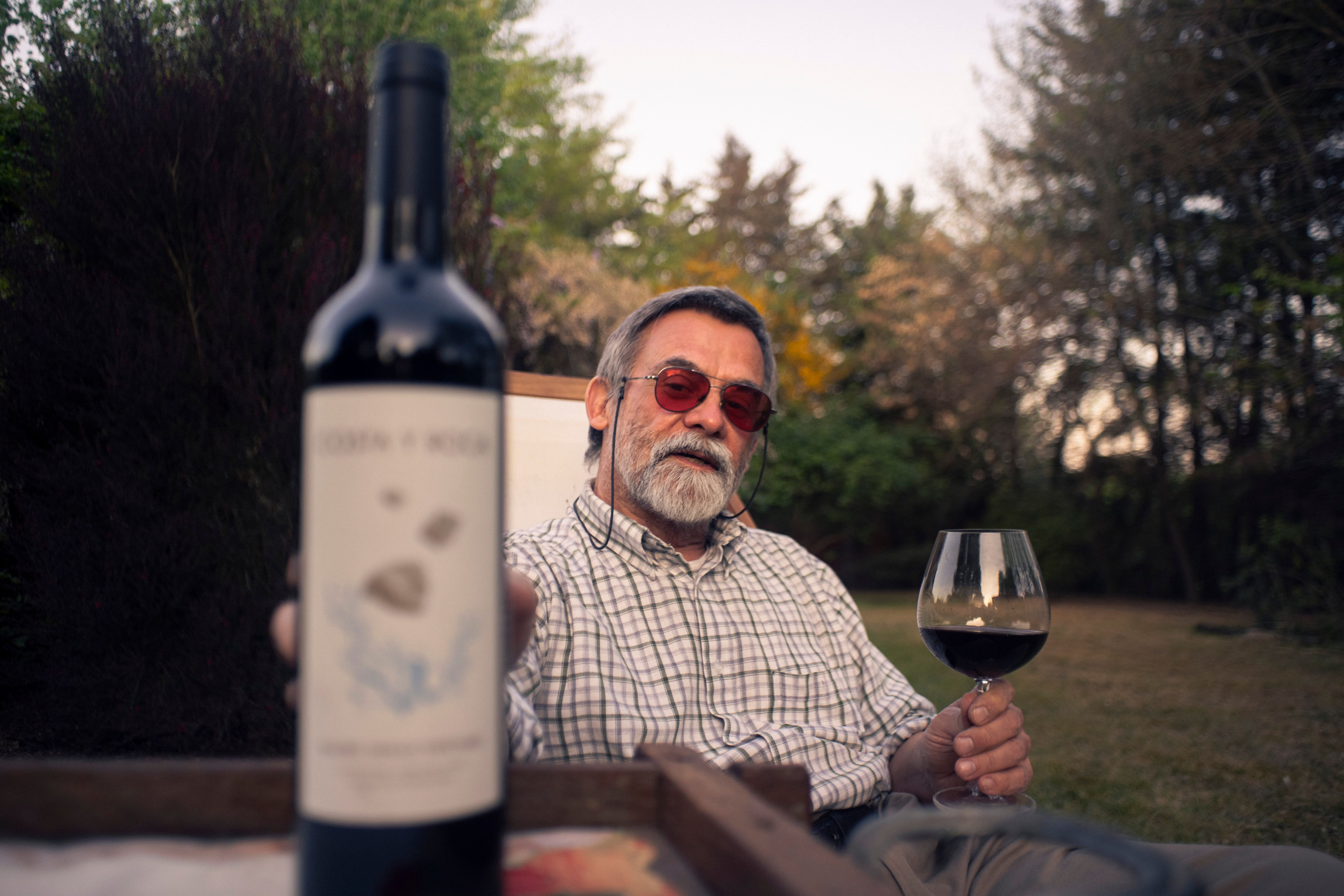 An adult man enjoying a glass of red wine in a tranquil garden setting during a warm day.