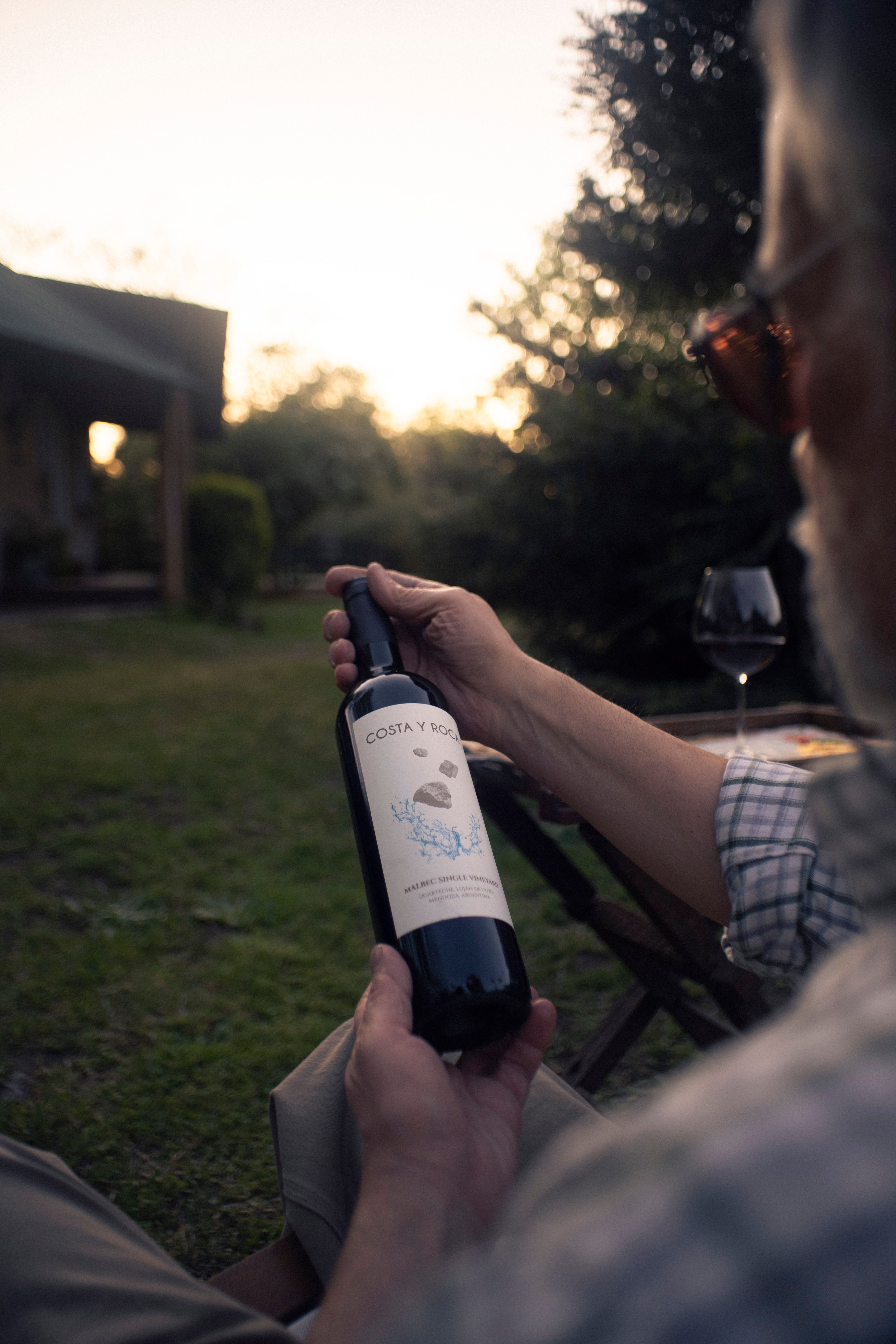 A person holding a wine bottle outdoors during sunset, evoking a relaxed atmosphere.