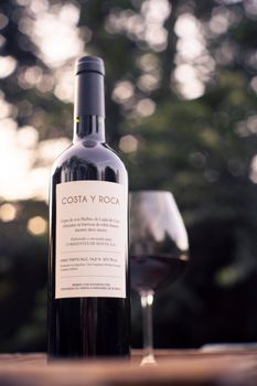 Close-up of Costa y Roca wine bottle with glass outdoors in natural light.