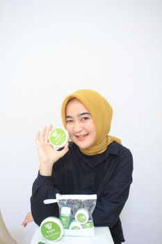 Smiling woman in hijab showcasing beauty products on a white background. - Fotografer Sidoarjo
