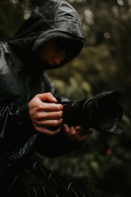 Close-up of a photographer in raincoat with a camera during rain.