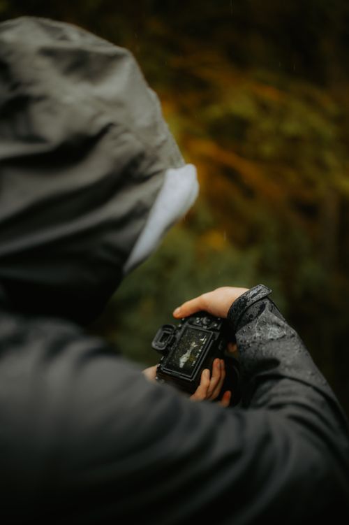 Free A photographer in a raincoat takes photos in a rainy setting, focusing on the viewfinder. Stock Photo