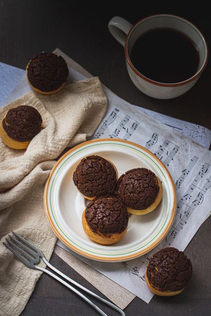 Overhead view of chocolate muffins on plate with coffee and music sheet.