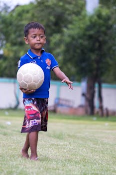 A young boy in a blue shirt playing soccer barefoot on a grassy field.