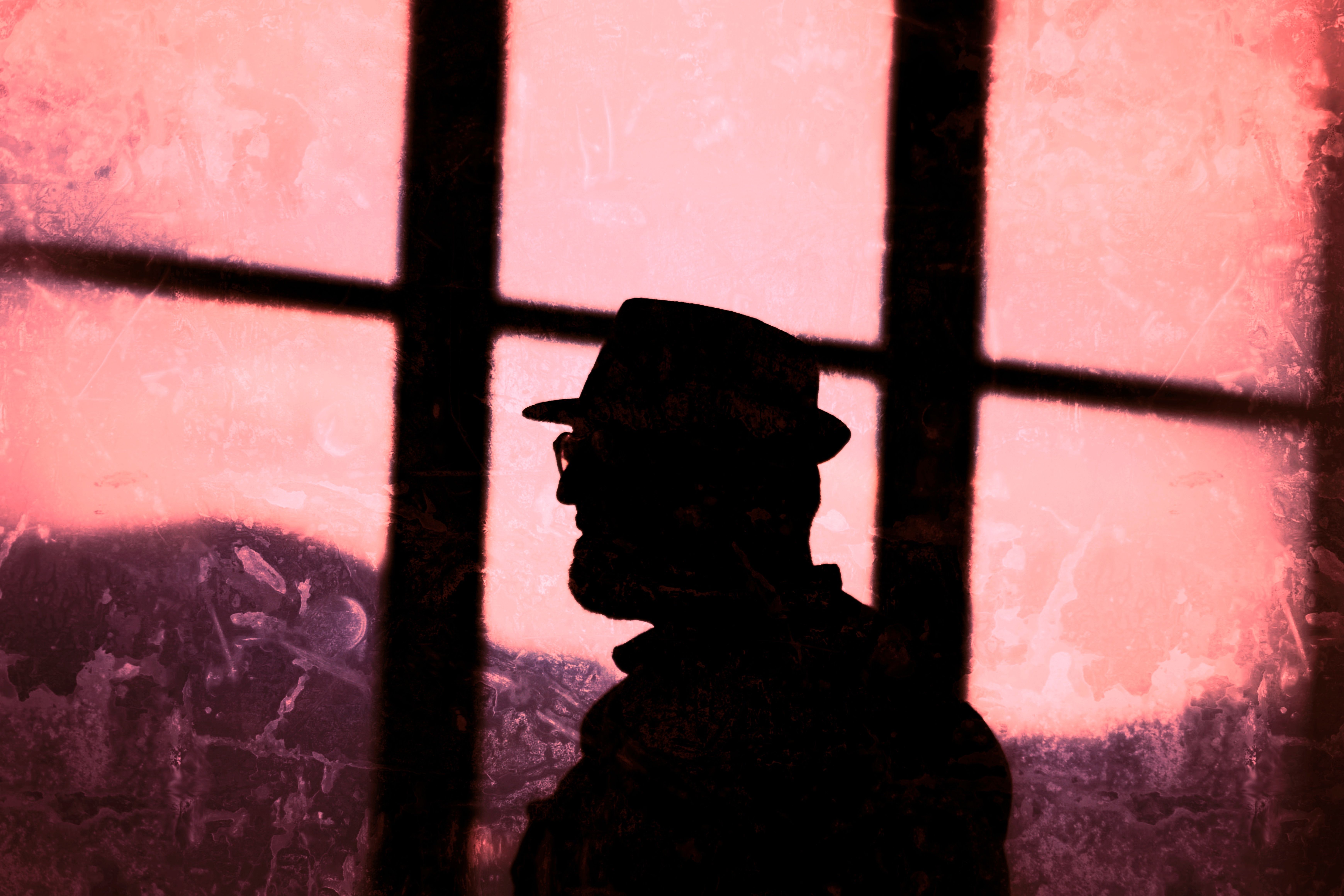 Mysterious silhouette of a man in a fedora, set against a textured pink background, evokes intrigue.