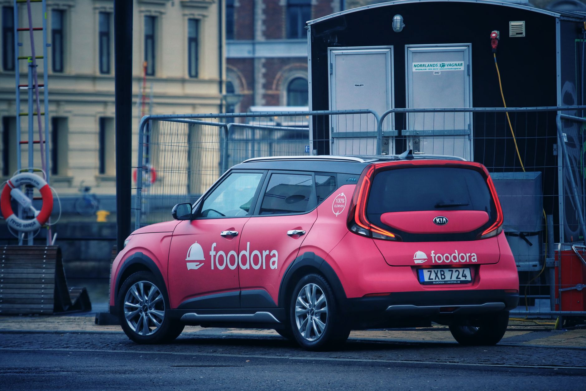 Pink electric vehicle from Foodora parked in an urban street setting in Sweden.