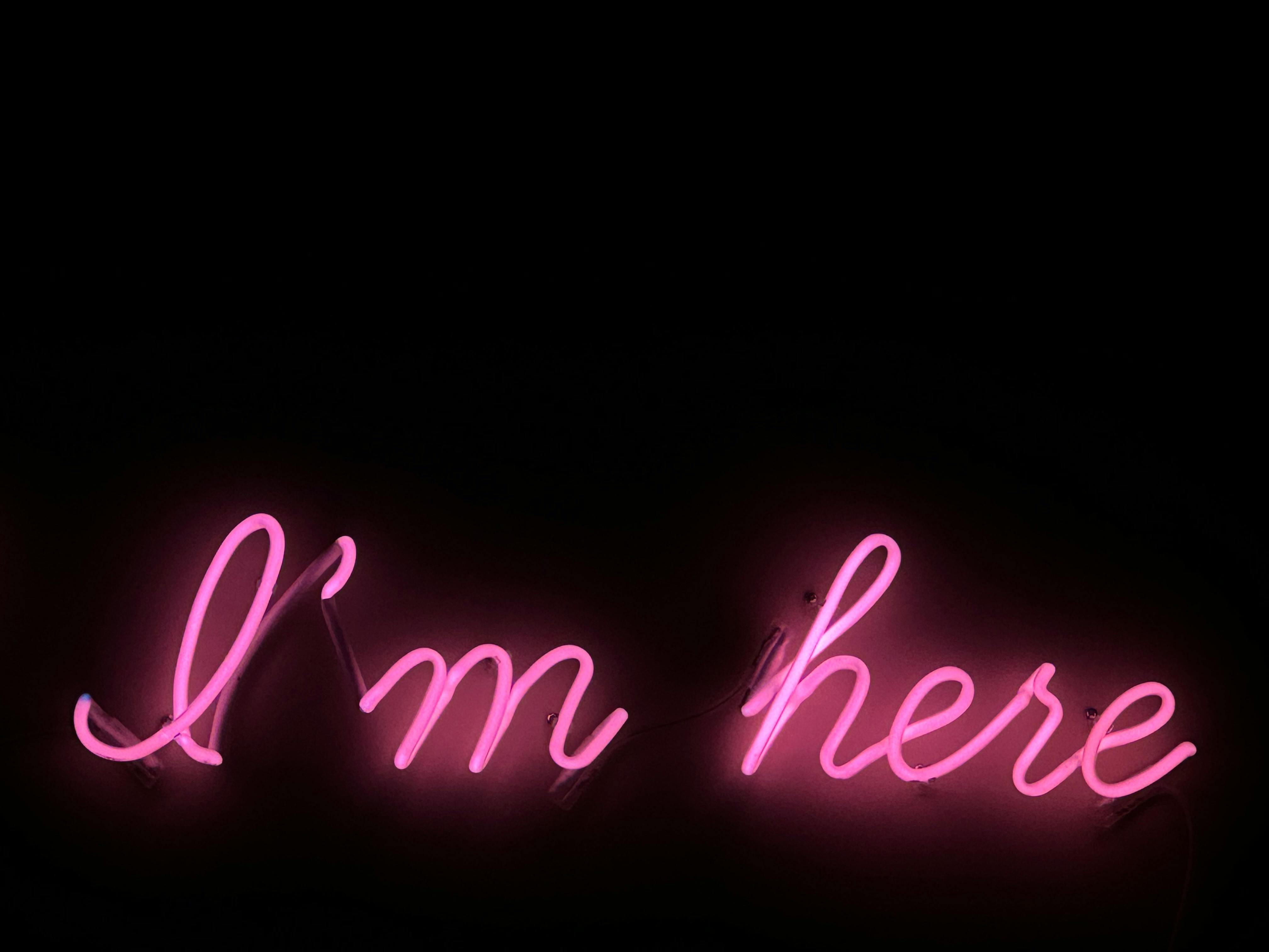 Vibrant pink neon sign reading 'I'm Here' against a dark background, perfect for modern designs.