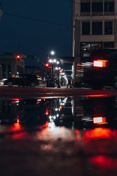 Evening city scene with car lights reflecting in a puddle on the street.