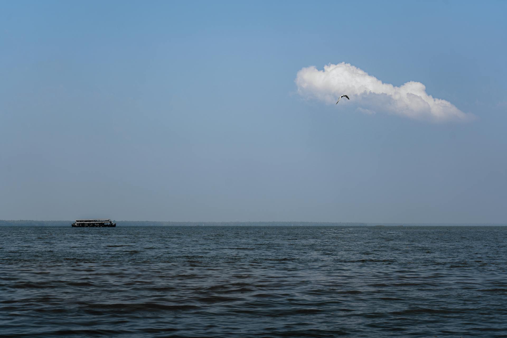 A serene boat journey on the backwaters of Alappuzha, India, under a clear blue sky and fluffy clouds.