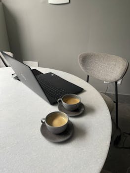 Tranquil office setup with laptop and two coffee cups on round table, ideal for productivity.