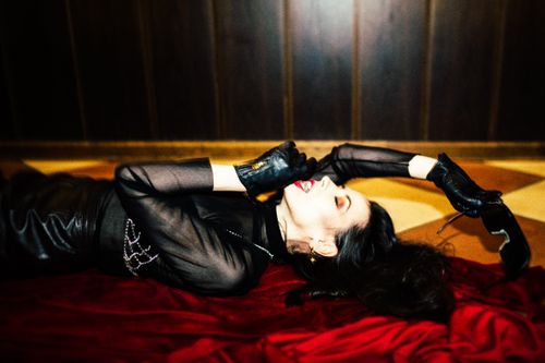 Free Stylish woman in black leather outfit lying on red fabric in dramatic pose indoors. Stock Photo