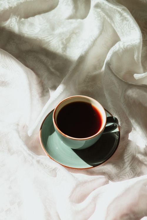 Free A green coffee cup on elegantly textured white fabric in calming natural light. Stock Photo