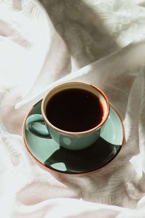 Free A light teal coffee cup filled with dark coffee resting on sumptuous fabric. Stock Photo