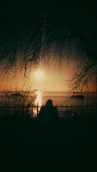 Silhouette of a person watching the sunset over the ocean with dramatic golden hues and reflections.