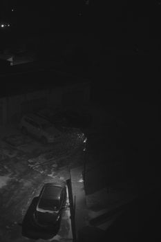 A dimly lit parking lot at night with snow gently falling, creating a serene winter scene.
