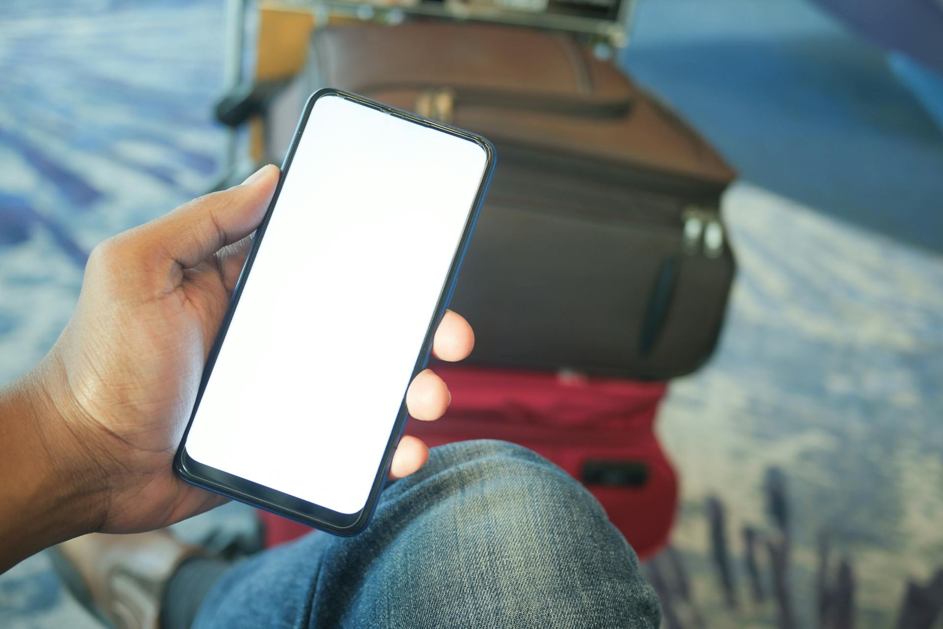 A person holding a smartphone in an airport with luggage visible, ideal for travel and tech concepts.