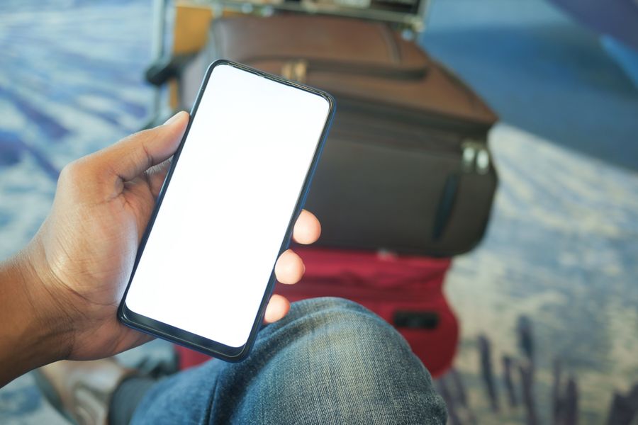 A traveler holding a smartphone with luggage beside them at an airport terminal