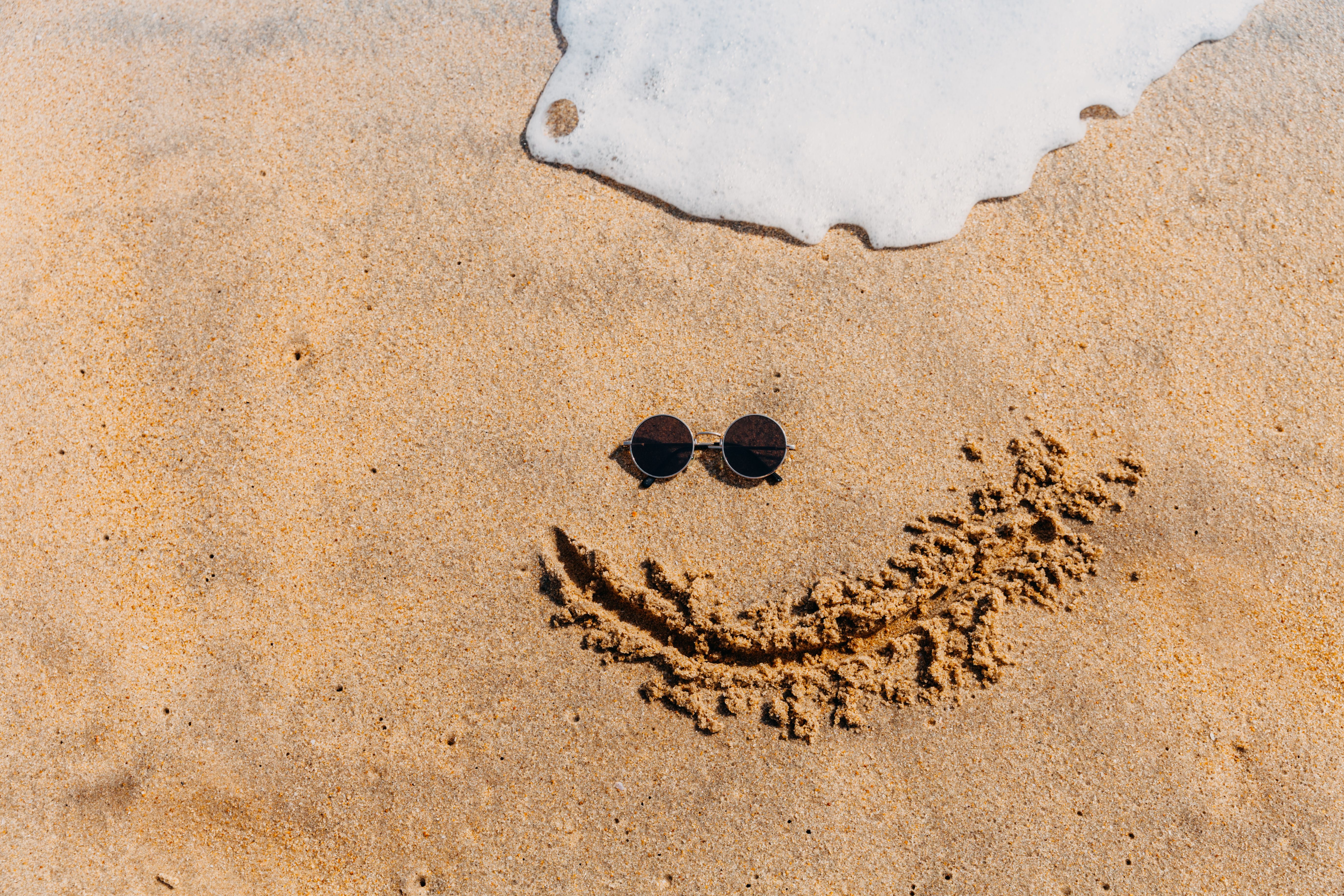 Sunglasses placed on sand with waves creating a summer vibe. Perfect for vacation themes.