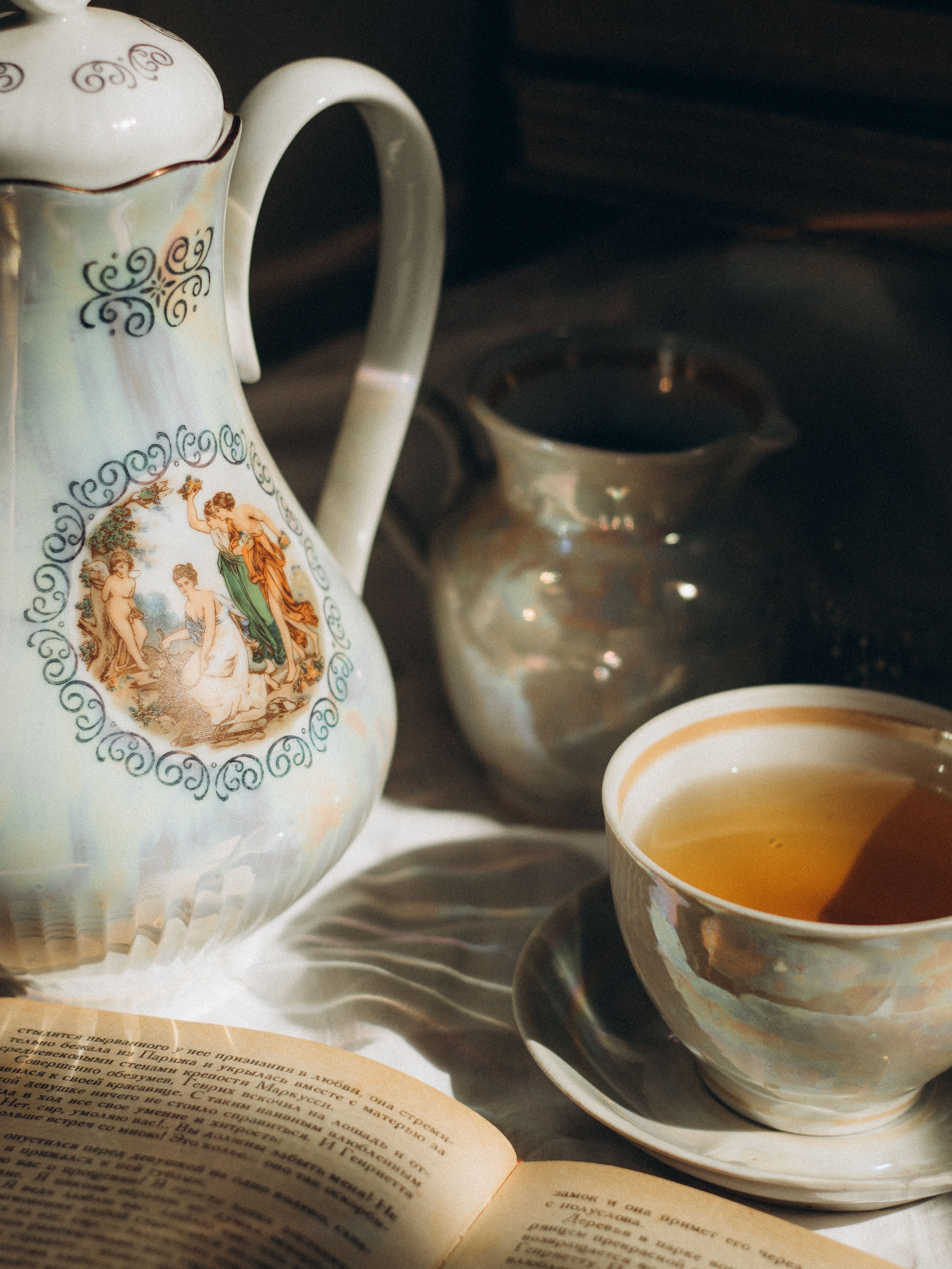 Elegant porcelain tea set with warm tea and open book in soft sunlight. Perfect cozy morning ambiance.