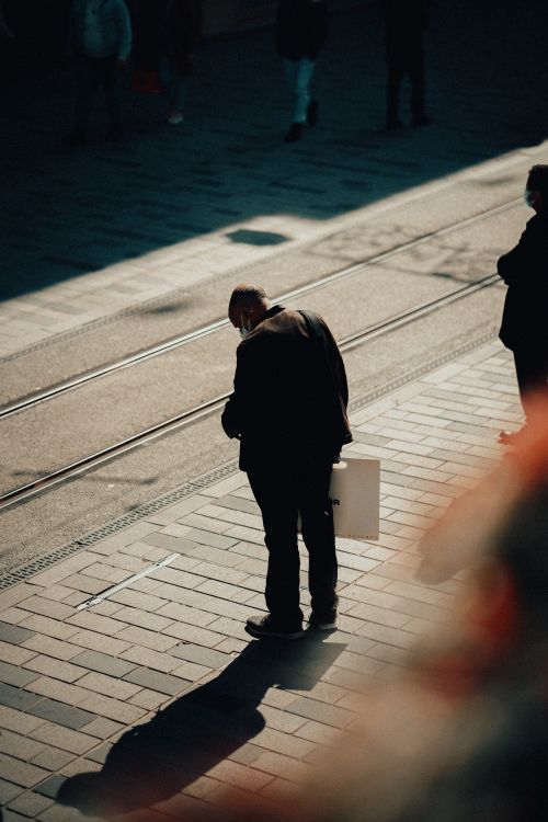 Free Man stands at tram stop in city, casting shadow on sunny day. Stock Photo