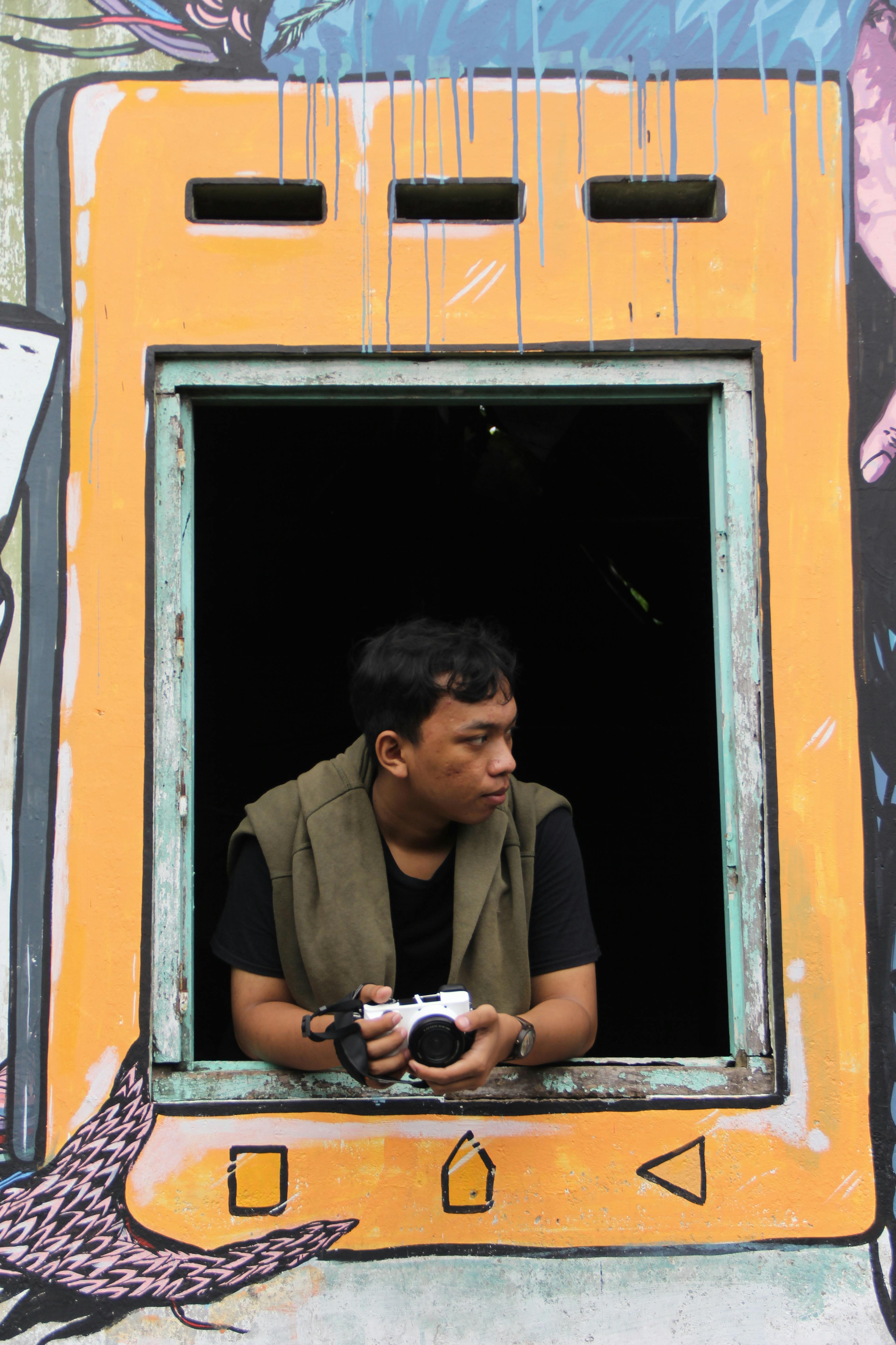 A man with a camera looks out from a window framed by colorful street art.