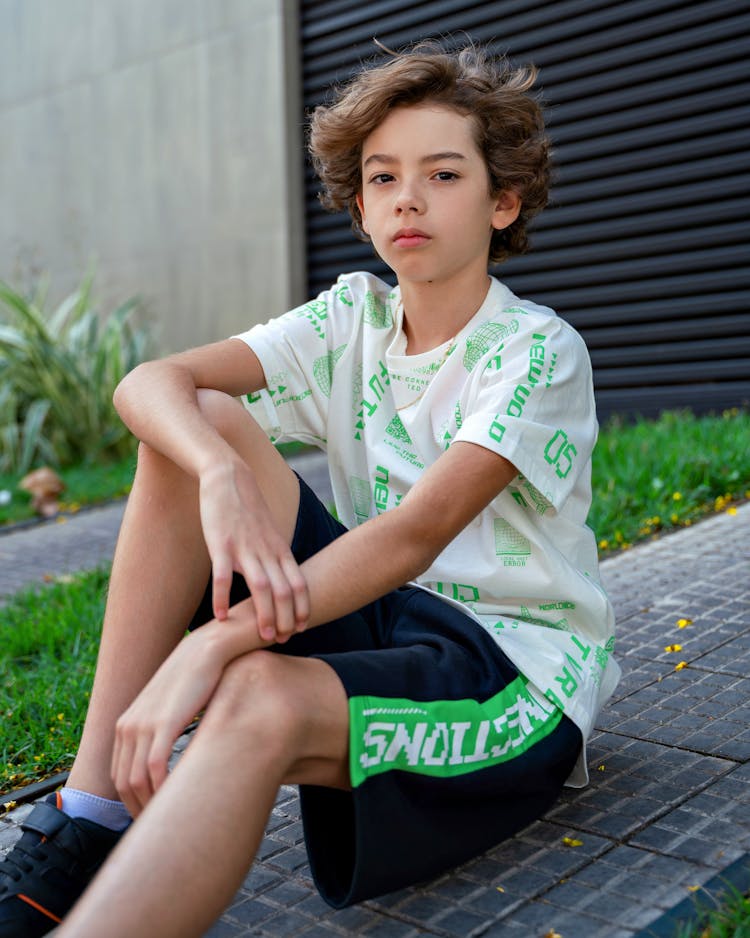 Boy In Sportswear Sitting On Ground Outdoors