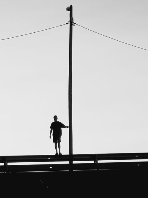 Free A silhouette of a man standing on a bridge with a pole under a clear sky. Stock Photo