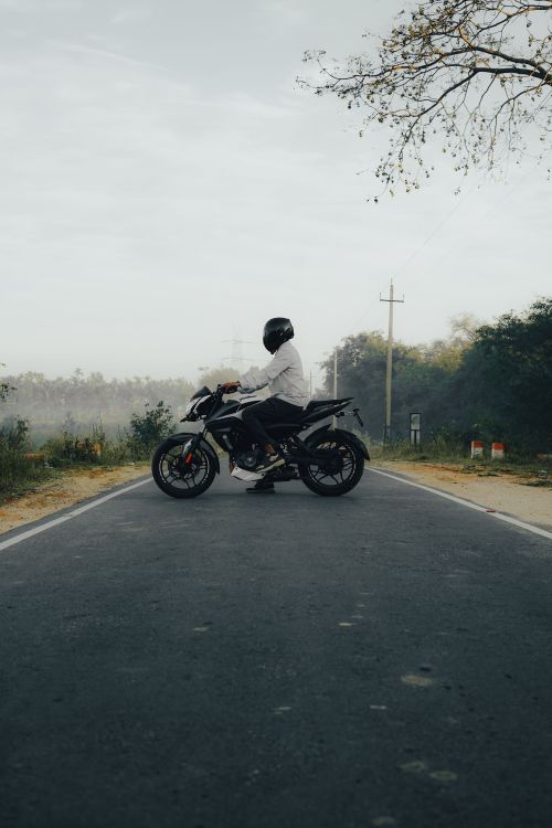 Free A lone motorcyclist in helmet rides down a misty rural road at dawn, surrounded by trees. Stock Photo