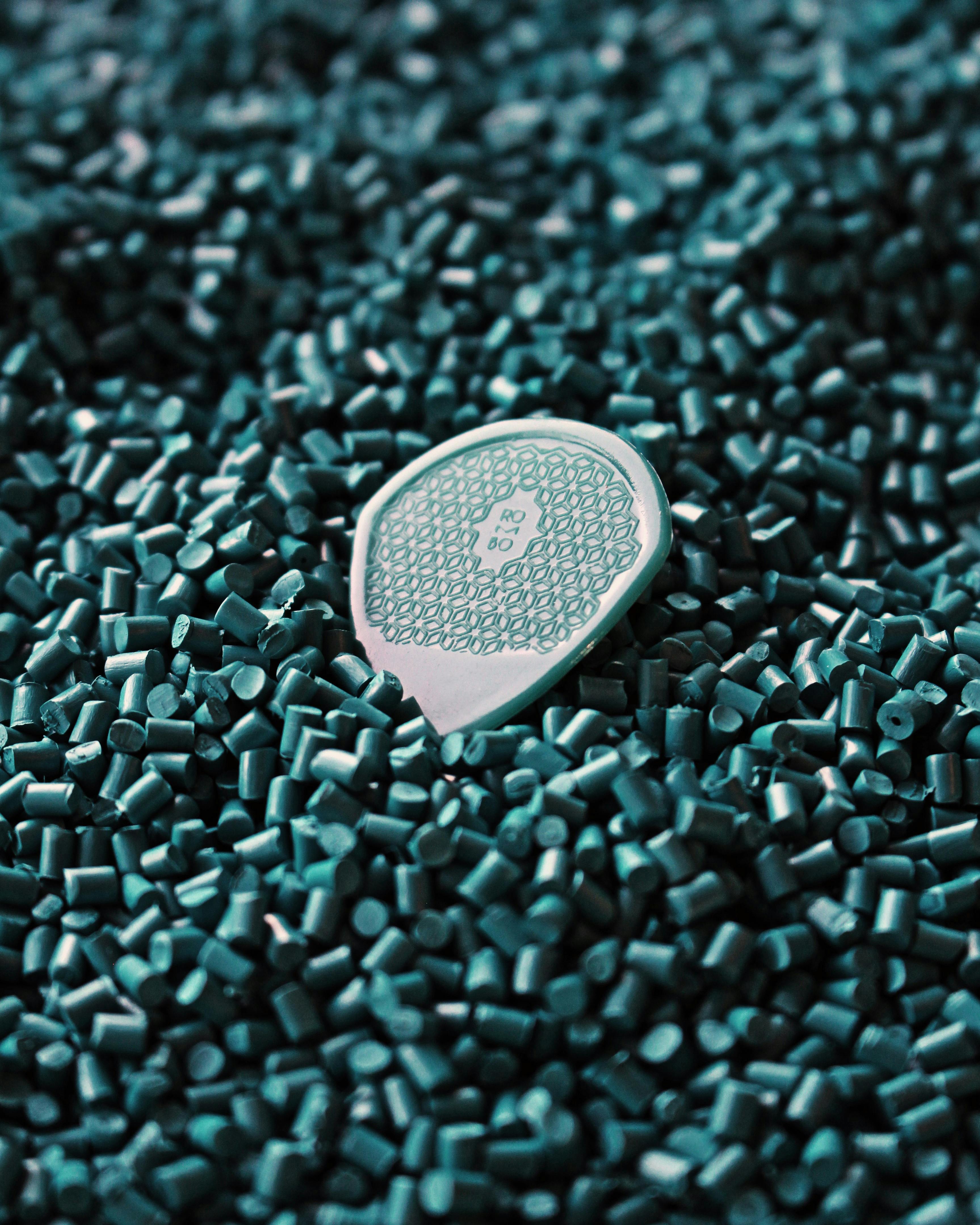 A detailed view of a green guitar pick surrounded by rubber granules, emphasizing texture and simplicity.