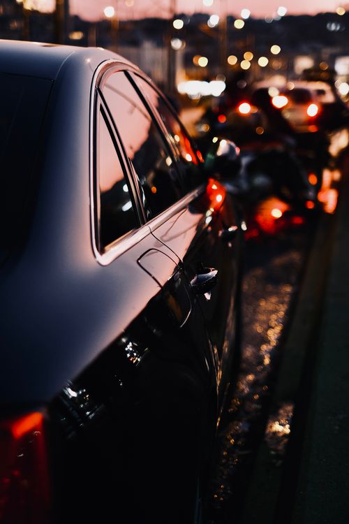 Free A sleek black luxury car with reflections at twilight in a busy city street. Stock Photo