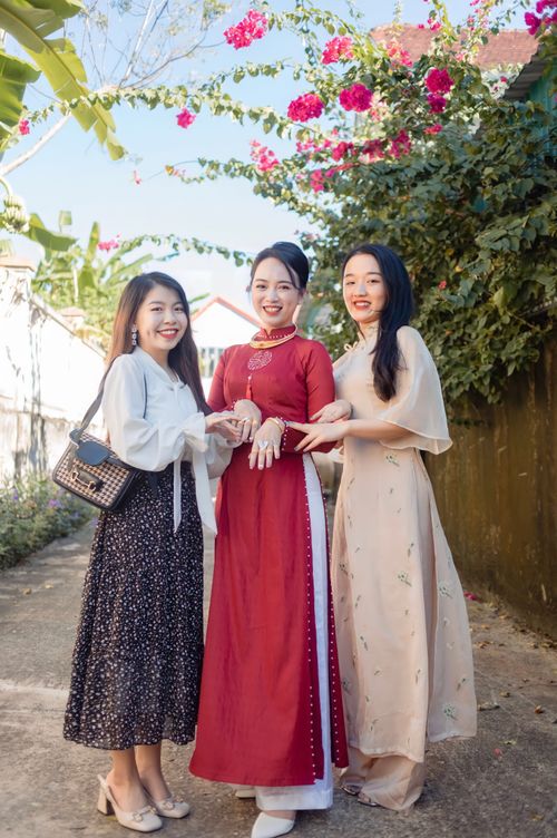 Free Three women in colorful Ao Dai dresses enjoying time together outdoors in a sunny setting. Stock Photo
