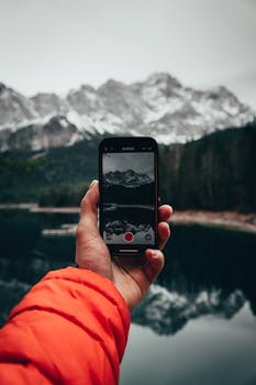 A scenic view of snow-capped mountains captured with a smartphone by a lake.