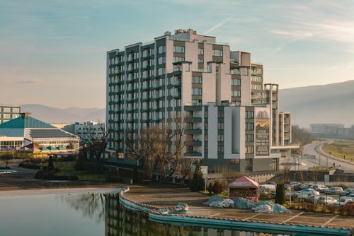 Free Explore a modern residential building with a serene pond and scenic mountain backdrop, ideal for urban living. Stock Photo