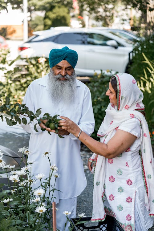 Photo of an Indian Couple in White Traditional Clothing Picking Fruits from a Tree