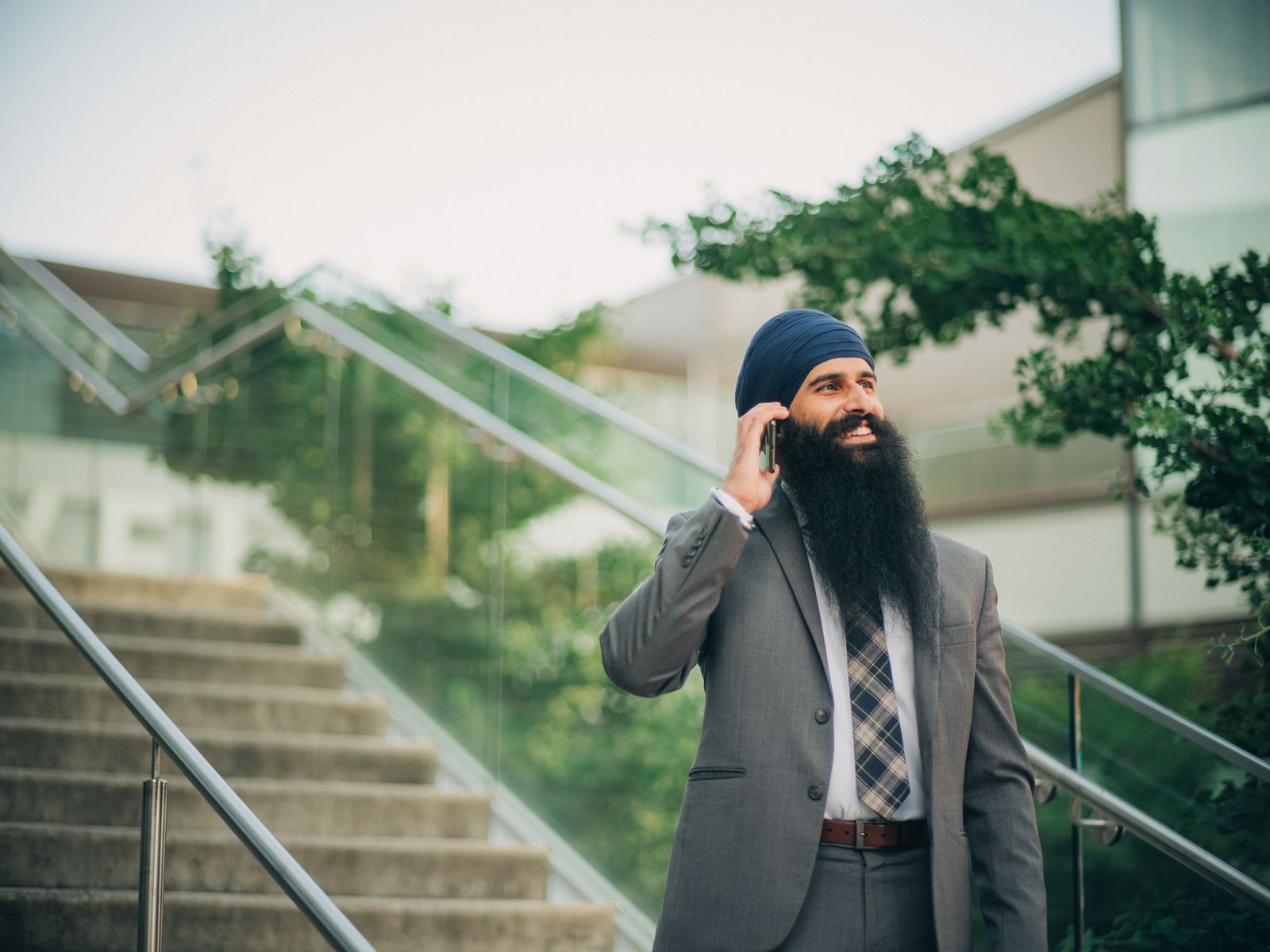 Smiling businessman with a beard and turban talks on phone outside on sunny day