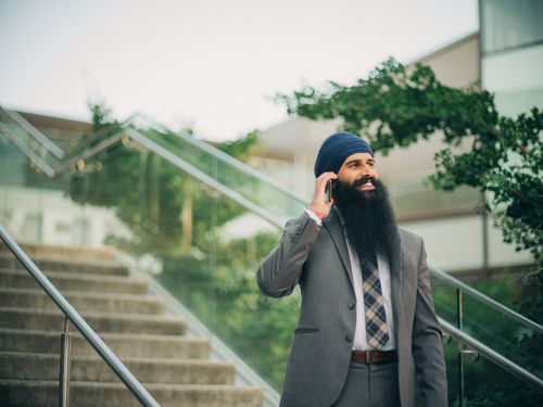 Free Smiling businessman with a beard and turban talks on phone outside on sunny day Stock Photo