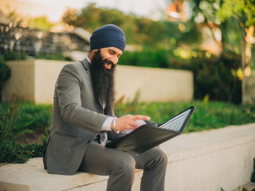 Man wearing business attire and turban reviews a portfolio outdoors, showcasing professionalism and focus. Man wearing business attire and turban reviews a portfolio outdoors, showcasing professionalism and focus.