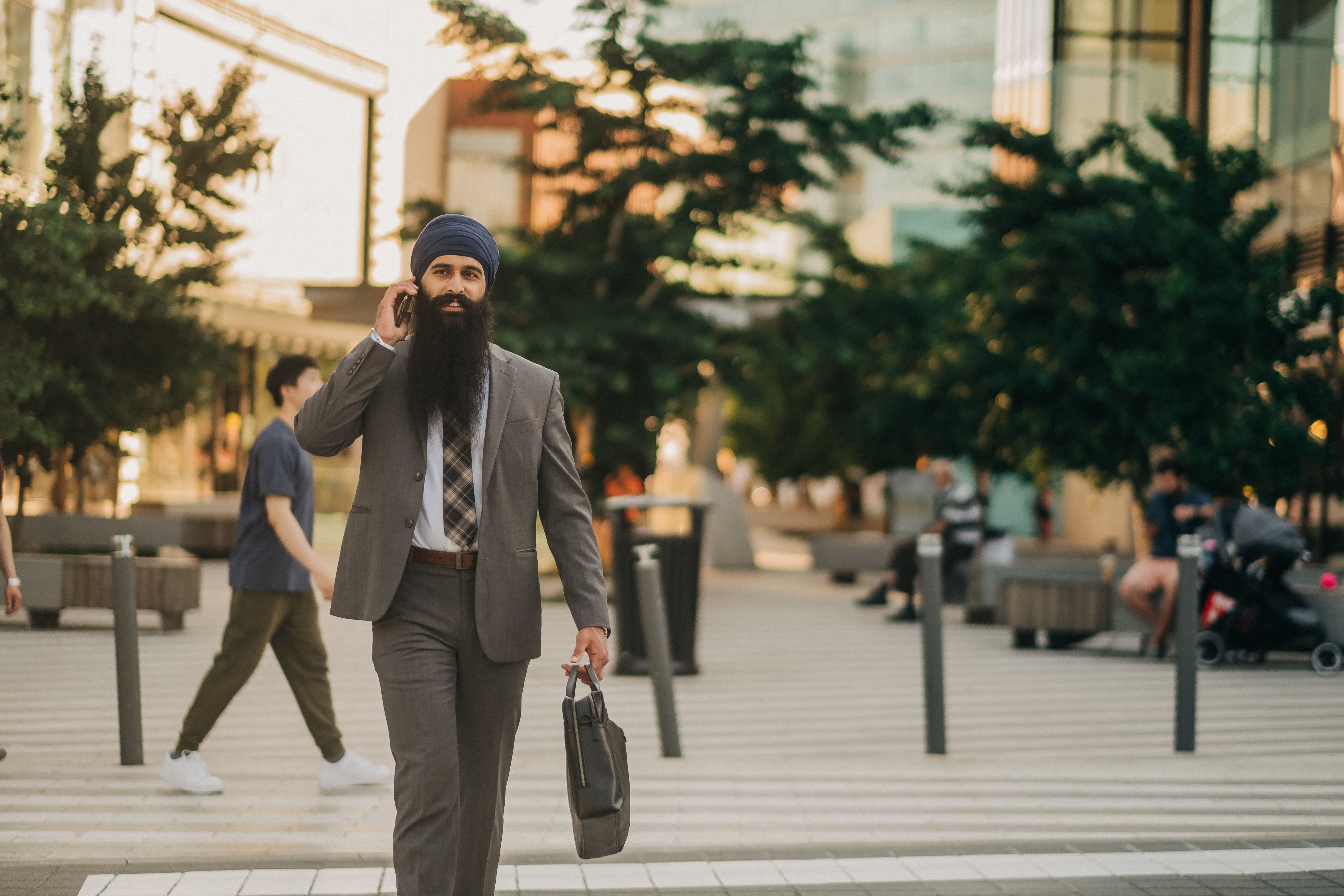 A businessman in a suit and turban walking confidently outdoors while talking on the phone.