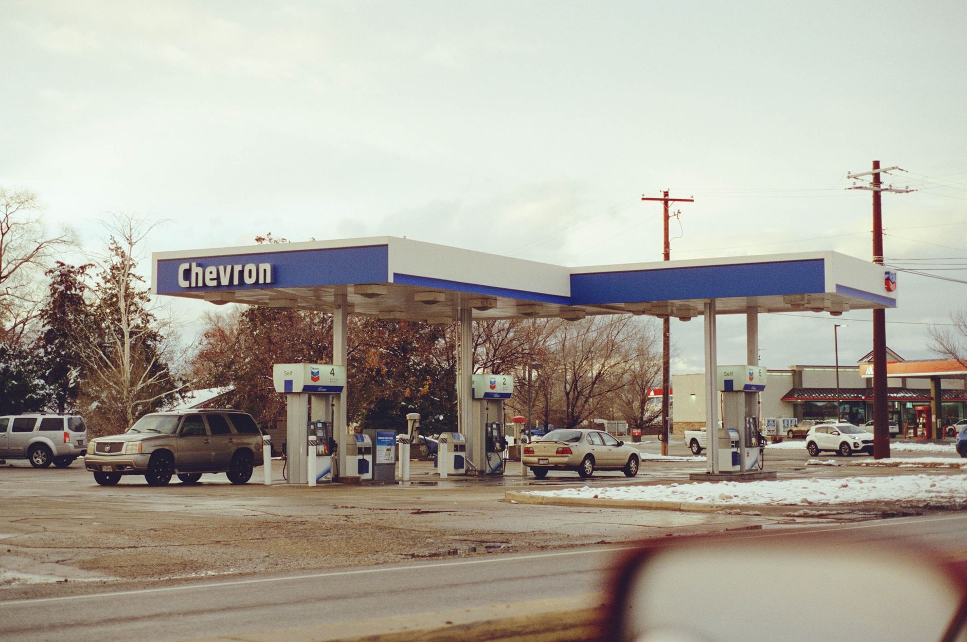 A Chevron gas station with several vehicles parked on a snowy day, emphasizing travel and fuel.