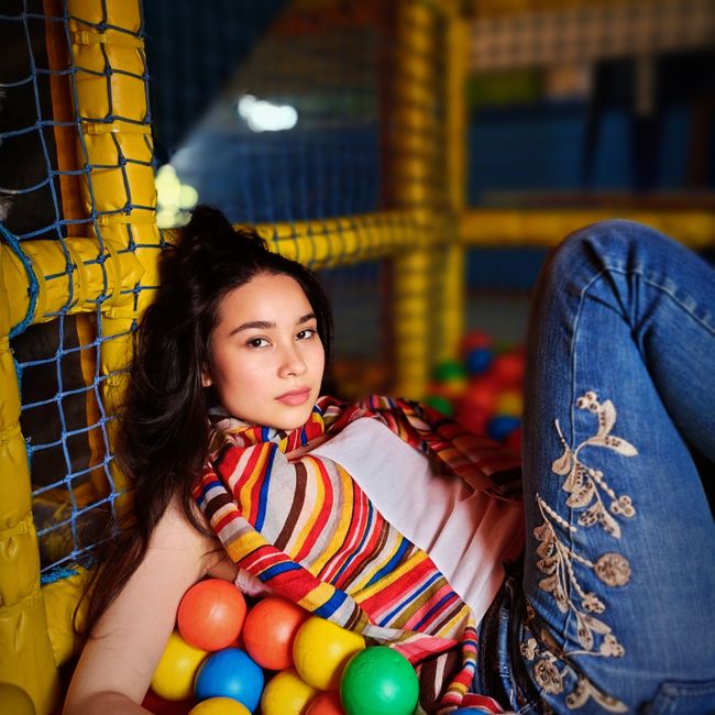 Fashionable young woman relaxing in a vibrant ball pit, exuding confidence.