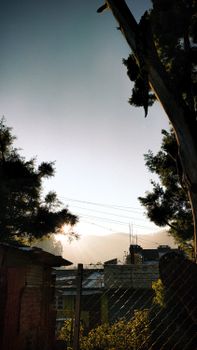 A serene sunrise casting a soft glow over a quiet mountain village, framed by trees.