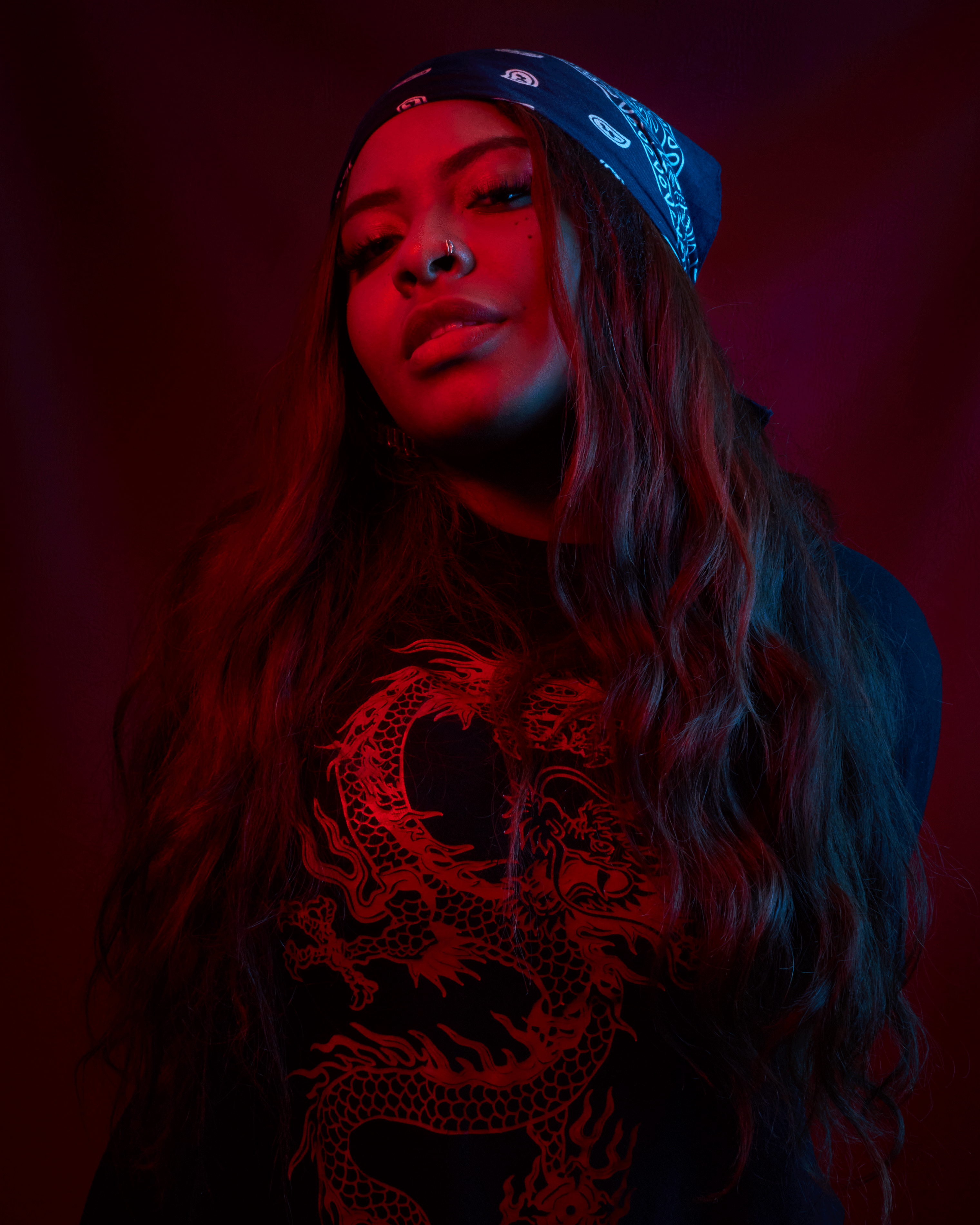 Moody portrait of a woman with a bandana and dragon t-shirt in red lighting.